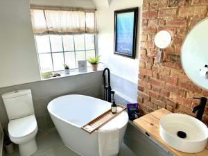 a bathroom with a white tub and a brick wall at Cooden Cottage in Bexhill