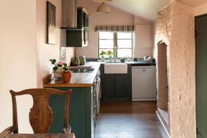 a kitchen with green cabinets and a wooden chair at Apple Cottage - Vivre Retreats in Wimborne Minster +22 photos