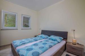 a bedroom with a bed with blue sheets and two windows at Apartment in Vrbnik - Insel Krk 47401 in Vrbnik
