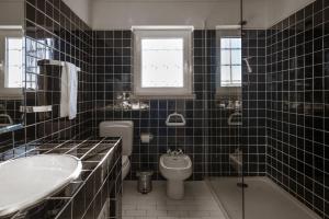 La salle de bains est pourvue de carrelage noir, d'un lavabo et de toilettes. dans l'établissement Casa do Magoito, à Bolembre de Baixo