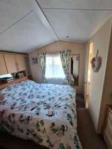 a bedroom with a bed with a floral bedspread and a window at Sea Shore Chalet - Rockley Park in Lytchett Minster