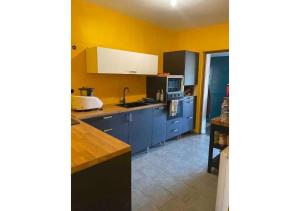 cocina con armarios azules y pared amarilla en Chambre tropicale privée, en Liévin