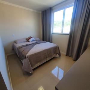een kleine slaapkamer met een bed en een raam bij Apartamento de Luxo com Piscina em Bombinhas in Bombinhas