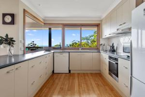 a kitchen with white cabinets and a large window at Sapphire Views - Narrawallee Beach in Narrawallee