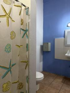 a bathroom with a shower curtain with seashells and a toilet at Wide Mouth Frog Conchal in Brasilito