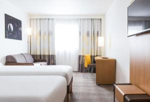 une chambre d'hôtel avec deux lits et un canapé dans l'établissement Novotel Saint-Quentin en Yvelines, à Magny-les-Hameaux