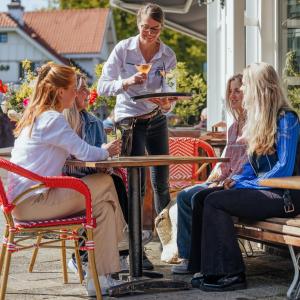 Eine Frau, die ein Tablett mit einer Gruppe Frauen am Tisch hält. in der Unterkunft Hotel Fase Fier Eten en Drinken in Castricum