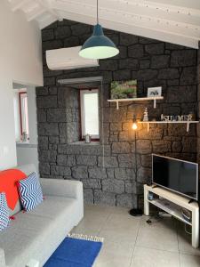 a living room with a stone wall with a couch and a tv at Cantinho dos Cagarros in Lajes do Pico