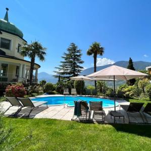 a swimming pool with chairs and an umbrella at Villa Hochland in Merano