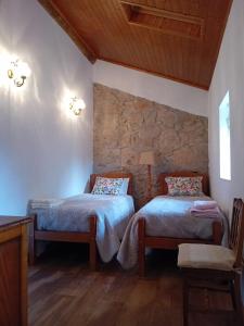 a bedroom with two beds and a stone wall at Casa do Loureiro in Ferrarias