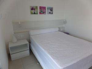 a small white bedroom with a bed and a nightstand at Mediterrane Residence in Aquiraz