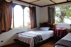 a small bedroom with a bed and two windows at INKA LAKE Taquile Lodge in Huillanopampa