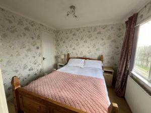 a bedroom with a bed with a pink comforter and a window at 2 Bedroomed Lodge with Private Garden in Penrith