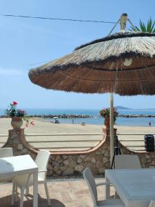 uma praia com um guarda-sol de palha e uma mesa e cadeiras em Tropical House em Formia