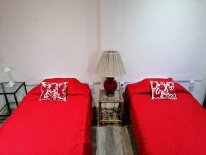 duas camas num quarto com lençóis vermelhos e um candeeiro em Los Huacales Apartamento em Oaxaca de Juárez