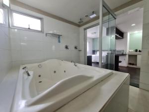a white bathroom with a tub and a window at Hotel San Diego Pampulha - Flats Particular in Belo Horizonte
