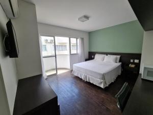 a bedroom with a white bed and a television at Hotel San Diego Pampulha - Flats Particular in Belo Horizonte