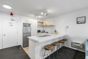 a white kitchen with a sink and a counter with stools at Beach Views at Oceanside in Mount Maunganui