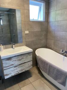 een badkamer met een bad, een wastafel en een spiegel bij Kingston Beach Home - Beach & Bush Views in Kingston Beach