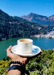 eine Person, die eine Tasse Kaffee vor einem See hält in der Unterkunft Sukoon Lake view BnB by Boho Stays in Nainital