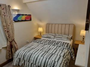 a bedroom with a bed with a striped bedspread and two lamps at Maryland Cottage Nr Gatwick in Godstone
