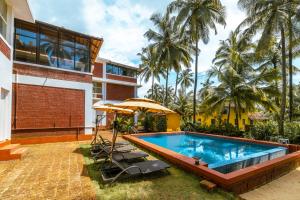 a swimming pool with chairs and an umbrella next to a building at Nilaya Stays in Padubidri