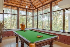 a man playing pool in a room with windows at Nilaya Stays in Padubidri