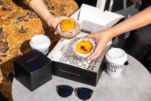 a person holding a donut on a table with two cups at Sage Hotel James Street in Brisbane