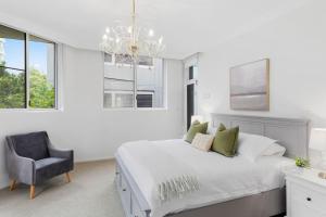 a white bedroom with a bed and a chair at Ocean Vista Escape - A Lofty Beachfront Penthouse in Wollongong