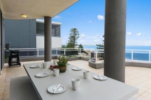 a white table with plates on it on a balcony at Ocean Vista Escape - A Lofty Beachfront Penthouse in Wollongong