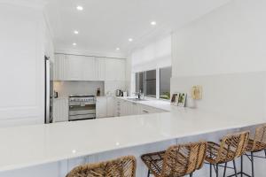 a kitchen with white cabinets and bar stools at Ocean Vista Escape - A Lofty Beachfront Penthouse in Wollongong