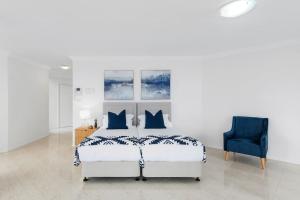 a white bedroom with a bed and a blue chair at Ocean Vista Escape - A Lofty Beachfront Penthouse in Wollongong