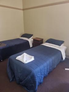 a room with two beds with blue sheets and a table at Coffs Harbour Hotel in Coffs Harbour
