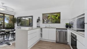 - une cuisine avec des placards blancs, une table et des chaises dans l'établissement Seaside Serenity Retreat, à Bellara