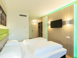 two beds in a room with a tv on a wall at B&B HOTEL Bochum-Hbf in Bochum