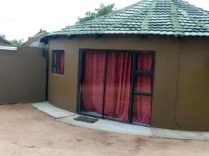 Casa pequeña con 2 ventanas con cortinas rojas en @ The Village Lodge, en Hazyview