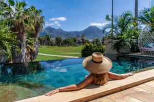 Eine Frau mit einem Strohhut, die neben einem Pool sitzt. in der Unterkunft Royal River, Luxury Hotel - Adults Only in Adeje