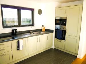 uma cozinha com armários brancos, um lavatório e uma janela em The Longhouse em Castle Douglas