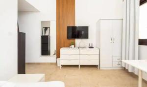 a white living room with a tv and a white dresser at Manzil - Studio Apartment in Dubai Silicon Oasis near Dubai Outlet Mall in Dubai