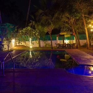 a swimming pool at night with a table and umbrellas at Fool's Paradise in Alleppey