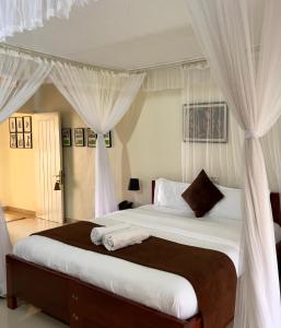 a bedroom with a large bed with white curtains at Sunset Hotel Entebbe in Entebbe