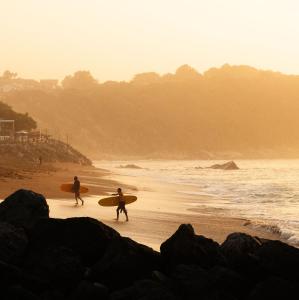 dos personas caminando por la playa con sus tablas de surf en Aparra Surfcamp Saint-Jean-de-Luz, en San Juan de Luz