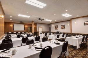 Travelodge by Wyndham Brandon في براندون: قاعة اجتماعات مع طاولات وكراسي وشاشة