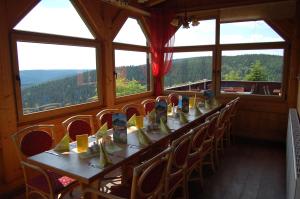 een lange tafel met stoelen in een kamer met ramen bij Berggasthaus & Pension Schöne Aussicht in Klingenthal