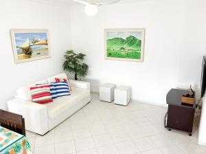 a living room with a white couch and paintings on the wall at PS5: Aproveite Ubatuba! Apto Completo & Bem Localizado in Ubatuba