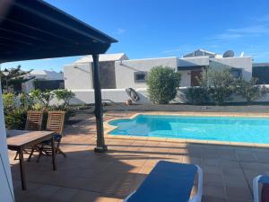 einen Pool mit Stühlen, einem Tisch und einem Sonnenschirm in der Unterkunft Faro Park Villa Bella heated Pool in Playa Blanca