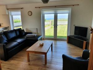 a living room with a black leather couch and a coffee table at Bayview 1-Bed Cottage in Isle of Lewis in Bragor