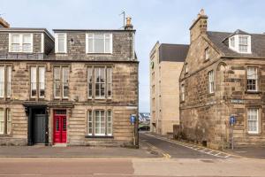 an old stone building with a red door on a street at Gibson Place - 15 Secs to The Old Course: Parking Nearby in St. Andrews