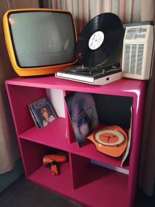 a pink shelf with a tv and a computer and a clock at Une pause en Provence au Village des antiquaires de la Gare in LʼIsle-sur-la-Sorgue
