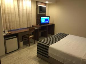 a hotel room with a bed and a desk with a computer at Palace Hotel Campos dos Goytacazes in Campos dos Goytacazes